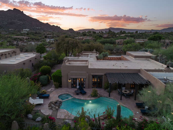 As evening falls, the estate glows against the desert landscape, showcasing its resort-style backyard and timeless Southwestern design.