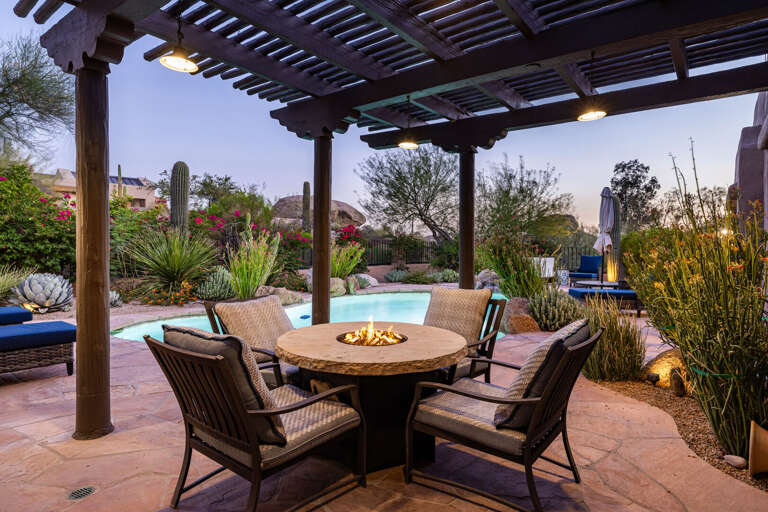 Gather around the fire table beneath the covered pergola—an inviting spot for evening conversations, cocktails, and cool desert nights.