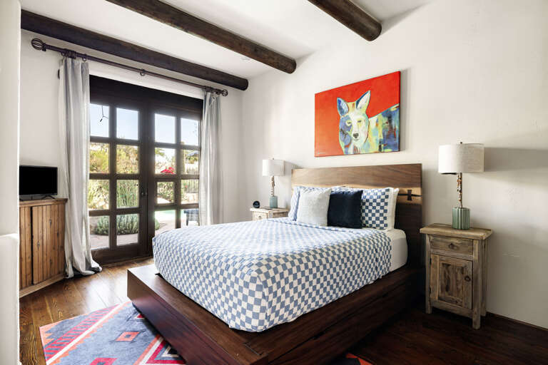 This inviting guest bedroom features a plush queen bed, French doors, hardwood floors, and abundant natural light for a relaxing stay.