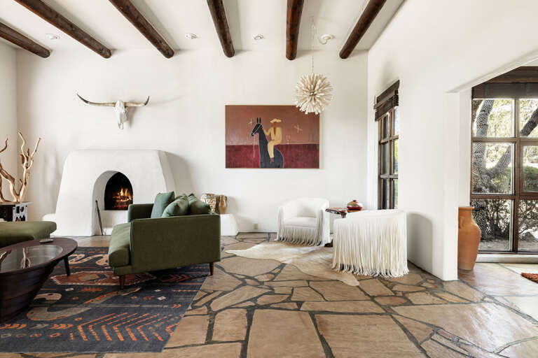 The open great room features a cozy fireplace, exposed wood beams, comfortable seating, and timeless Southwestern design.