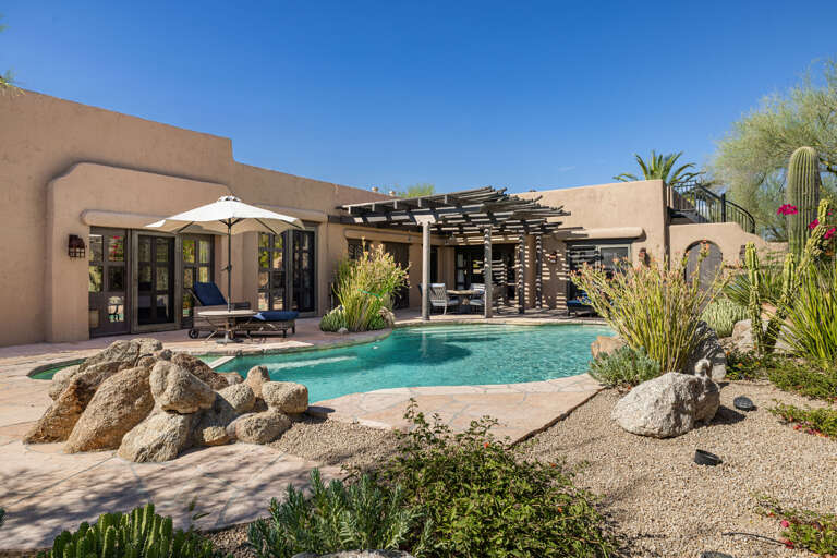 Relax beside the sparkling pool surrounded by lush desert landscaping, shaded patios, and multiple outdoor spaces for entertaining.