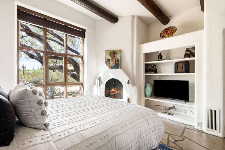 A welcoming guest bedroom with a plush queen bed, fireplace, custom built-ins, and large windows that fill the space with natural light.