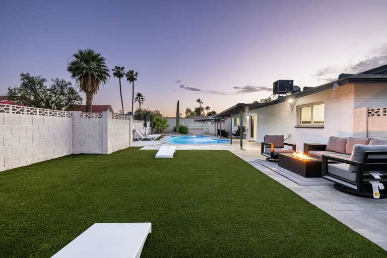 Beautiful sunset view of the spacious backyard featuring lawn games, outdoor seating, and poolside ambiance.