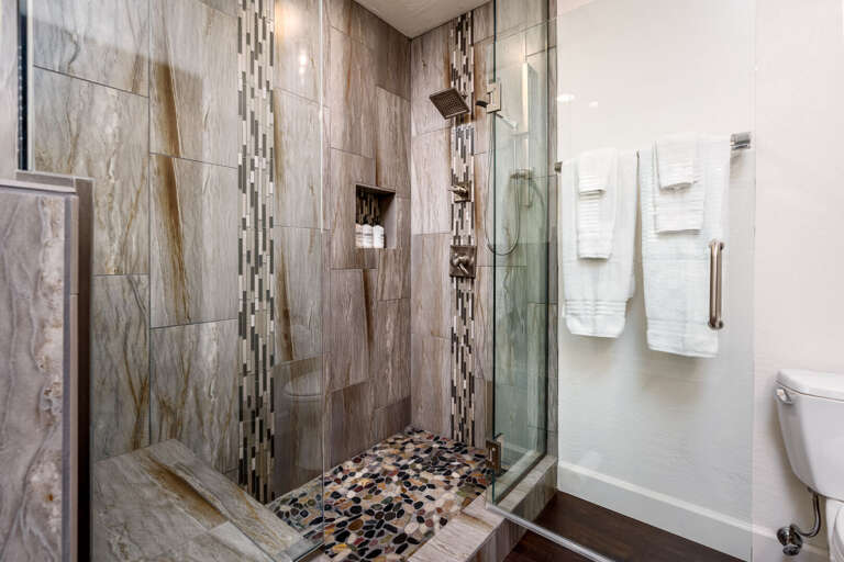 Indulge in a spa like shower experience with custom tilework, a rainfall showerhead, and elegant designer finishes.