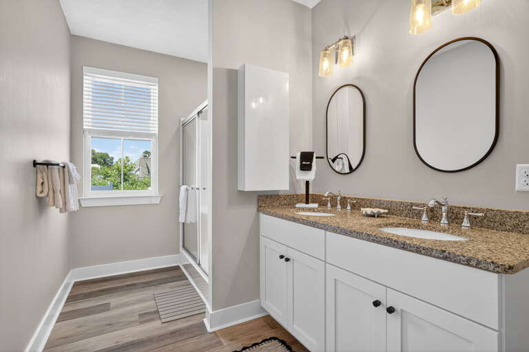 Primary bedroom ensuite bathroom featuring a glass walk-in shower, dual sinks and a privacy door separating the toilet.