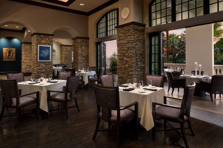 Polished Dining Space With Tables Set For Service, Stone Columns And Large Windows
