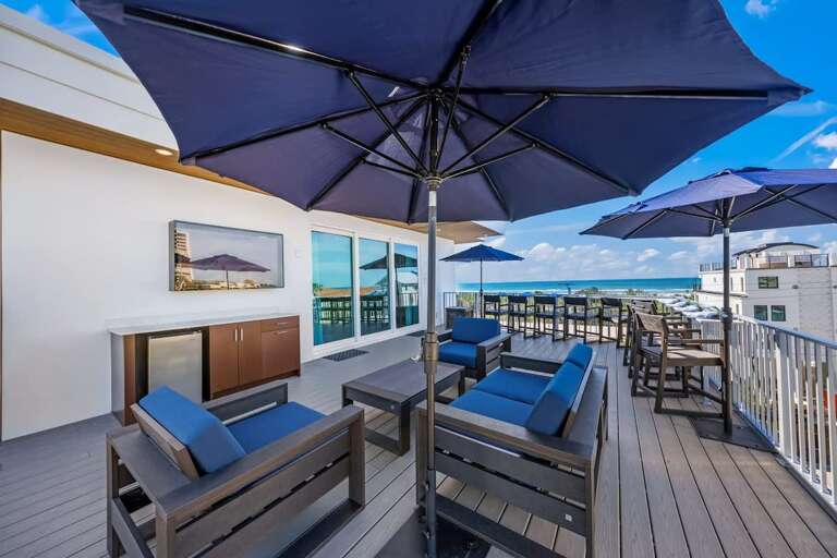 Rooftop Seating Under Blue Umbrellas Beside Beach View