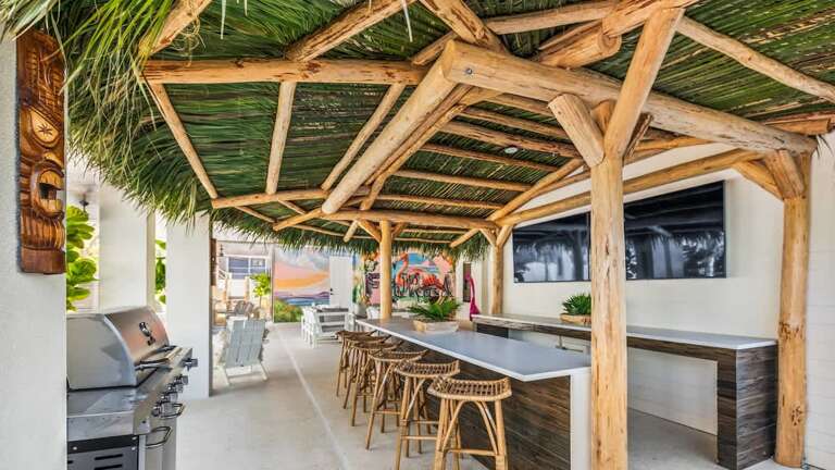 Thatched Roof Over Rustic Wooden Bar With Stools Beside Sunny Seating Area