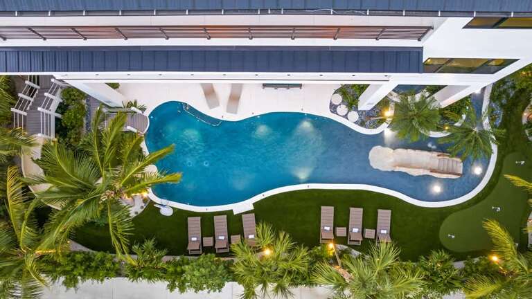 Aerial View Of A Serpentine Swimming Pool Surrounded By Palm Trees At A Vacation Rental