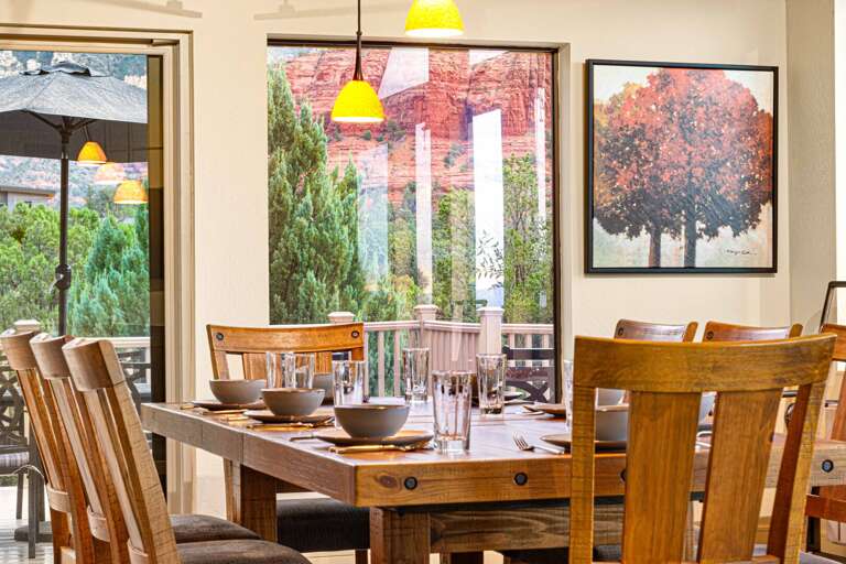 Wooden Dining Area With Yellow Lights, Lush Garden View Through Window, Set Table With Bowls Wooden Dining Area With Yellow Lights, Lush Garden View Through Window, Set Table With Bowls