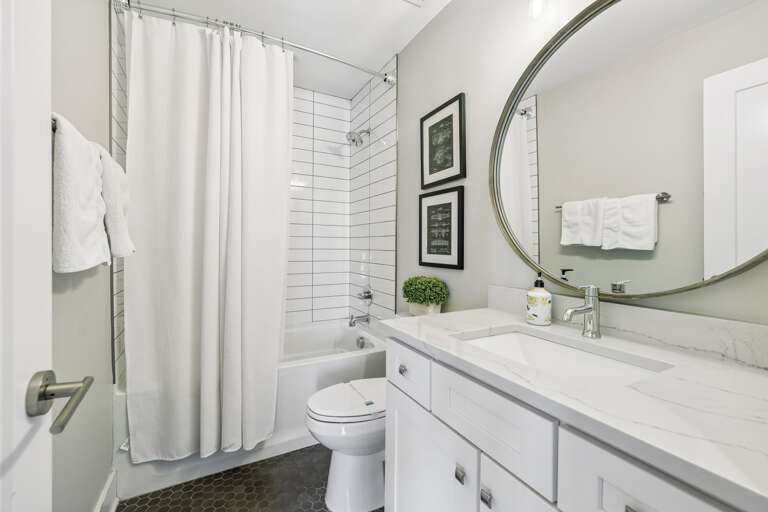 Subway tiled shower and tub combo behind a soft white curtain for a clean, classic look - Bright vanity with quartz counter &amp; chrome fixtures offers style &amp; functionality - Pops of color from fresh tulips and hex tile floor add personality and war
