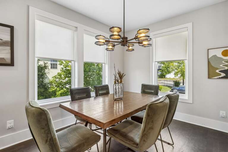 Light filled corner dining room with large windows and sleek contemporary layout - Olive green velvet chairs surround a warm wood table under a sculptural light fixture - Perfect for meals, board games, or casual coffee with natural sunlight all day