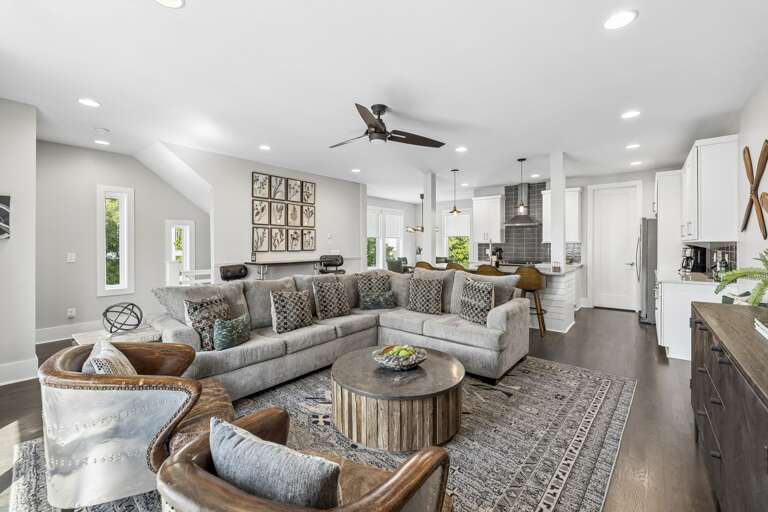 Spacious layout with plush sectional, bar seating, and sleek kitchen all in one view - Modern ceiling fans, warm wood tones, and leather accents enhance the cozy vibe - Perfect for entertaining, relaxing, or enjoying movie nights with friends and family