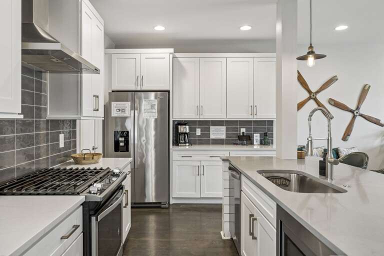 Full gourmet setup with stainless steel appliances, gas range, and large center island - Chic pendant lights, neutral tile backsplash, and extra counter space for easy prep - Wine and snack board welcome you into this stylish, functional culinary space