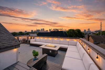 Cozy up around the firepit on this stylish rooftop with wraparound sectional seating - Panoramic city views under cotton candy skies create a magical evening atmosphere - String lights, stylish furnishings, &amp; skyline charm set the perfect sunset scene
