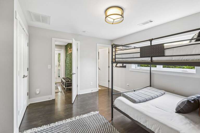 Stylish queen over queen bunk bed, dressed in modern striped linens - Includes a sleek desk, wall mounted TV, and tall mirror for comfort and convenience - Monochrome rug and minimalist décor create a polished, cozy sleep and work space
