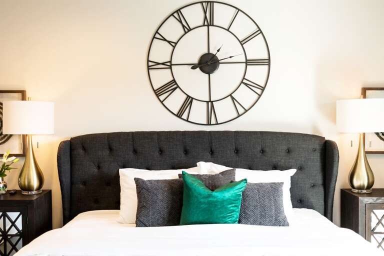 - Rich green accent pillow stands out against dark charcoal and crisp white linens - Statement headboard and modern decor create a luxe yet inviting sleep environment - Golden hour lighting highlights textures and cozy layers for a restful vibe