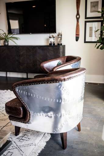 - Sleek leather armchairs with metal rivet accents add vintage aviation inspired character - Polished metallic backrests &amp; rich brown leather bring texture &amp; style to the space - Positioned perfectly for conversation or TV viewing in the living ar