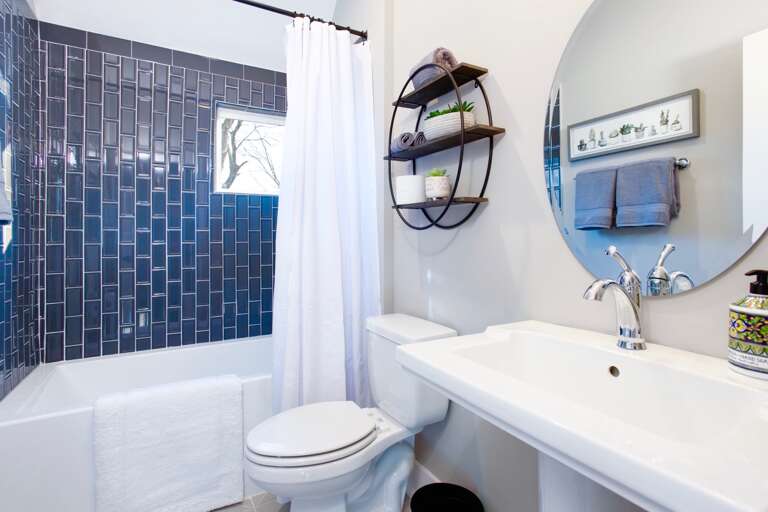 - Clean lines and bold navy tile give this bathroom a modern, refreshing feel - Round mirror, open shelving, and thoughtful touches make it both stylish and functional - Perfect for freshening up after a day out or unwinding with a relaxing soak