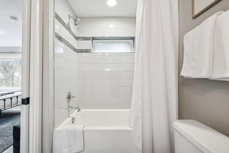 - Clean lines and bright white tile give this bathroom a modern, refreshing feel - Round mirror, open shelving, and thoughtful touches make it both stylish and functional - Perfect for freshening up after a day out or unwinding with a relaxing soak