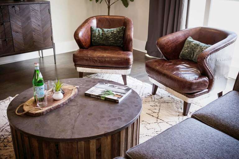 - Sink into vintage charm with these cozy leather accent chairs, perfect for morning coffee or evening chats - Textured round coffee table brings earthy style and space to gather around - Styled with books, bubbly, &amp; greenery for a warm, inviting touc