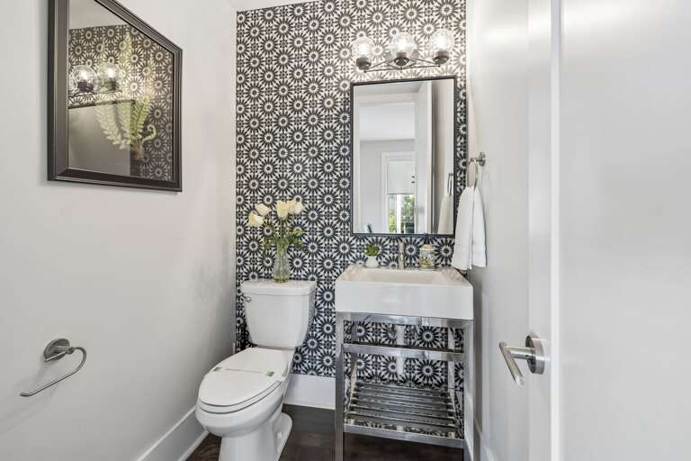 Eye catching black and white floral tile adds personality to this half bath - Sleek chrome vanity with open shelf and bold mirror elevate the modern vibe - Fresh florals, gold accent bin, and minimal décor create a polished guest space