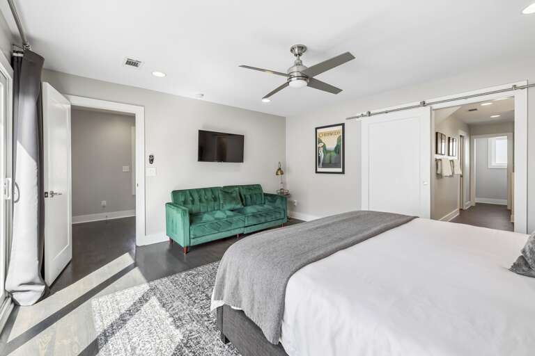 Emerald green tufted sofa adds a vibrant pop of color to this spacious bedroom lounge - Wall mounted TV and large windows make this a great spot for relaxing or streaming - Sophisticated black out drapes and detailed rug complete the room’s upscale feel