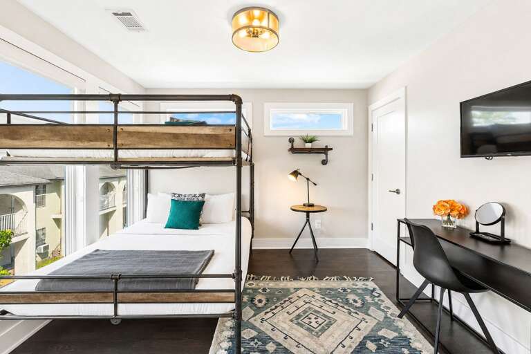 Industrial style queen over queen bunk bed, styled in cozy neutrals - Bright room with oversized windows, geometric rug, and desk setup for work or study - Thoughtful decor with greenery, light wood accents, and clean minimalist lines