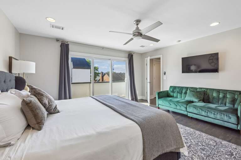 Emerald green tufted sofa adds a vibrant pop of color to this spacious bedroom lounge - Wall mounted TV and large windows make this a great spot for relaxing or streaming - Sophisticated black out drapes and detailed rug complete the room’s upscale feel
