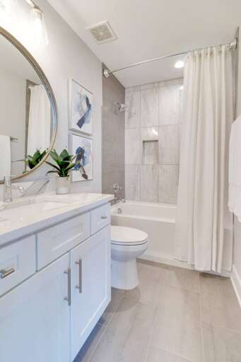 - Modern vanity with quartz countertop, chrome fixtures, and a circular mirror accent - Shower and tub combo surrounded by sleek marble tile with built in niche for ease - Artistic touches and greenery add a fresh and elegant vibe to this spa-like space