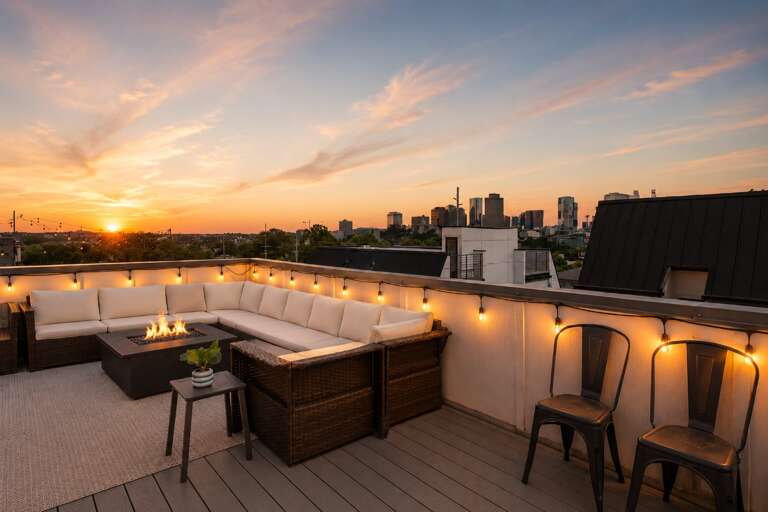 Step back and take in the full rooftop — fire pit, dining table, string lights, and skyline views that makes the whole thing feel like a private venue.