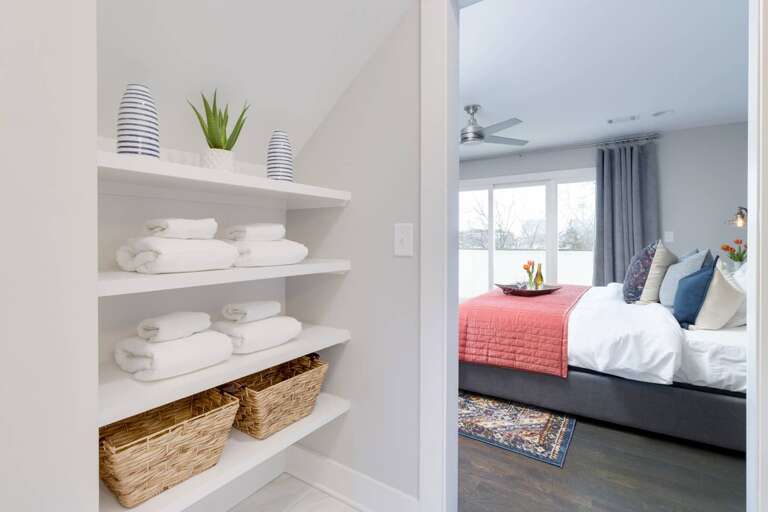 - Neatly stacked towels and woven baskets offer convenience right outside your bedroom door - Open shelving adds charm and function to this thoughtfully designed nook - Step into a cozy bedroom with a plush bed and vibrant decor accents
