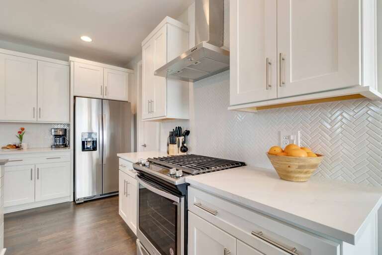 - All white cabinetry and quartz counters blend beautifully with herringbone backsplash - Stainless steel appliances, gas range, and coffee station ready for guest convenience - Clean lines and thoughtful layout make cooking or snacking a delight