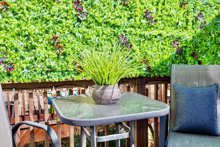 - Unwind on this stylish patio featuring a glass top bistro table and cozy cushioned chairs - Vibrant green plant wall creates the perfect backdrop for morning coffee or evening chats - Enjoy fresh air, comfort, and privacy in this serene nook