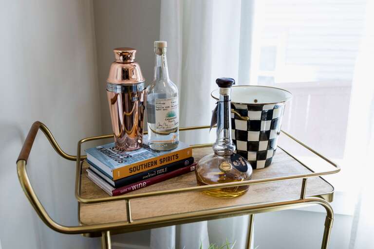 - Shake up something special with this chic bar cart stocked for your arrival - Stylish spirits, craft books, and a copper shaker invite you to unwind in style - Playful setup perfect for happy hour, nightcaps, or entertaining