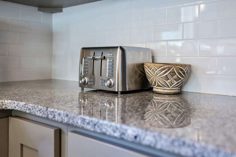 - Sleek stainless steel toaster ready for your morning bagels or artisan toast - Set against a polished granite counter and glossy white tile backsplash - Decorative stoneware bowl adds a cozy, curated kitchen feel