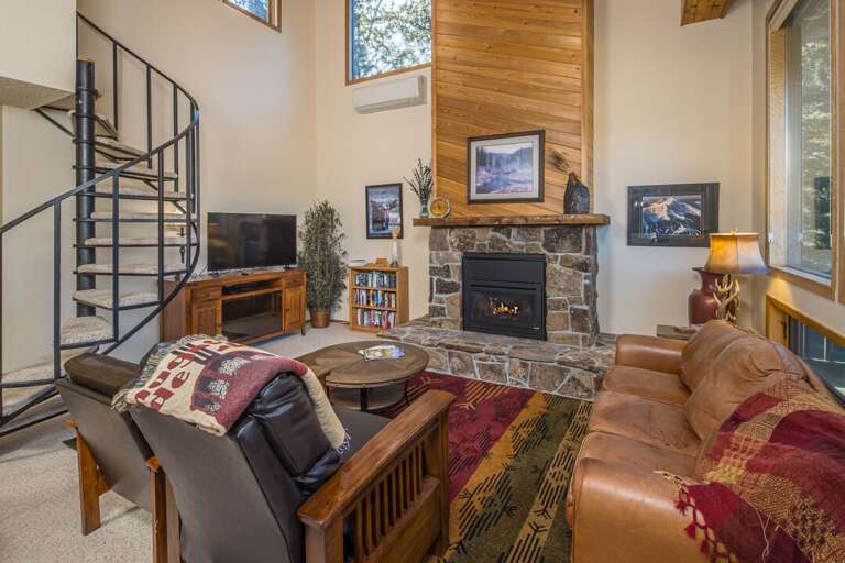 Rustic Room With Rounded Spiral Staircase, Sizable Windows, And Stone-lined Fireplace