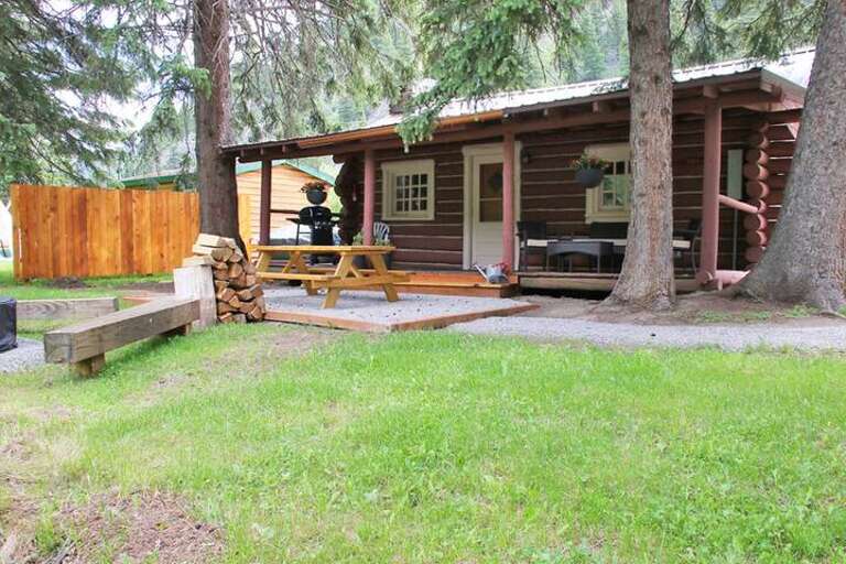 Backside of the cabin with covered porch, picnic table, and fire pit just steps away from the Gallatin River.