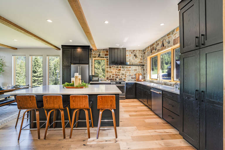 Spacious Kitchen With Stone Walls, Wooden Floors, And Black Cabinets