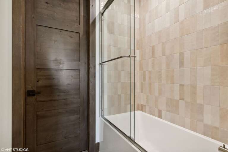 The ensuite for the guest bedroom offers a custom tile shower & tub | Main Level