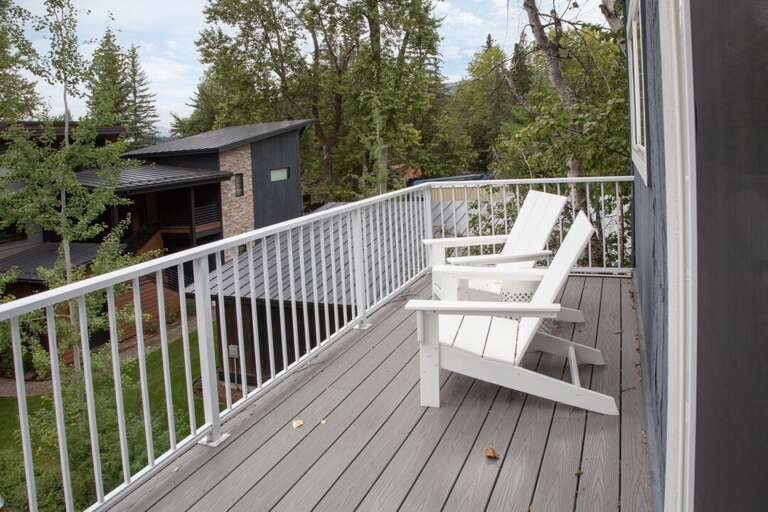 White Chair Waiting On Woody Deck, Leaf Litter, Lush Green Backdrop