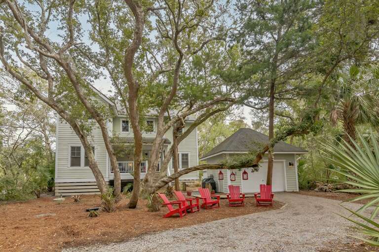 Vacation Rental Nestled Under Gnarled Oaks With Vibrant Red Chairs On A Gravel Drive