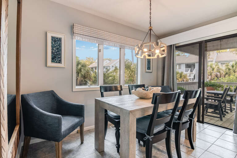 Vacation Rental Dining Area With Wooden Table And Chairs, Adjacent Outdoor Seating Visible Through Sliding Glass Doors