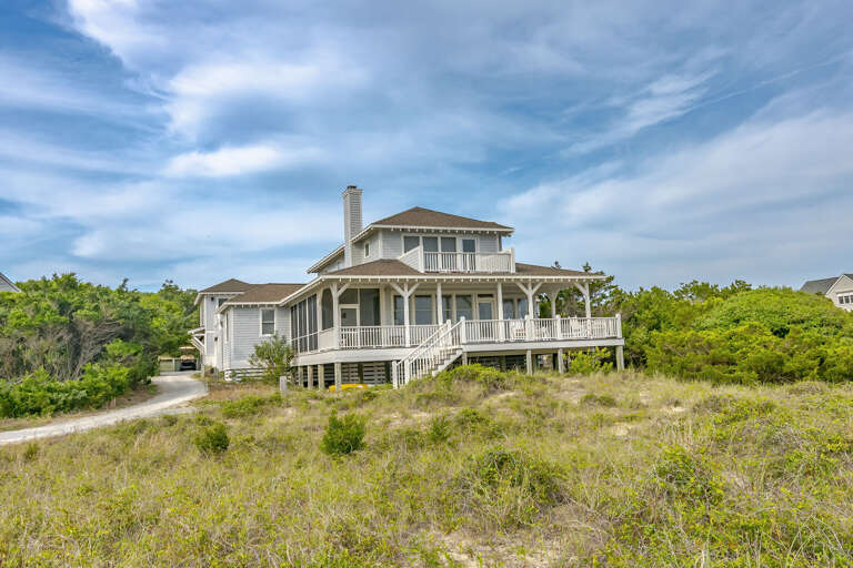 Seaside Structure Surrounded By Sand And Shrubs Under A Sweeping Sky