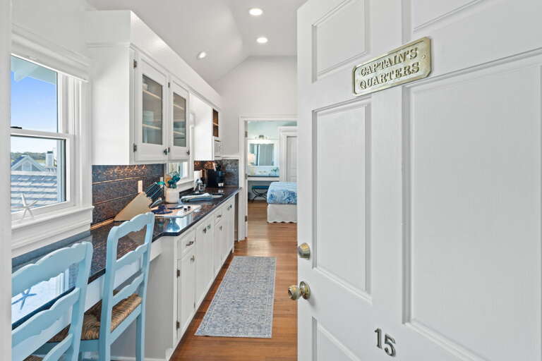 Interior View Showing White-walled Kitchen Leading To Blue-accented Bedroom, Labeled Captains Quarters In Vacation Rental