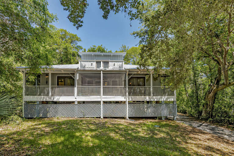 White Wooden Building With Wide Wrapped Porch Nestled In Lush Greenery