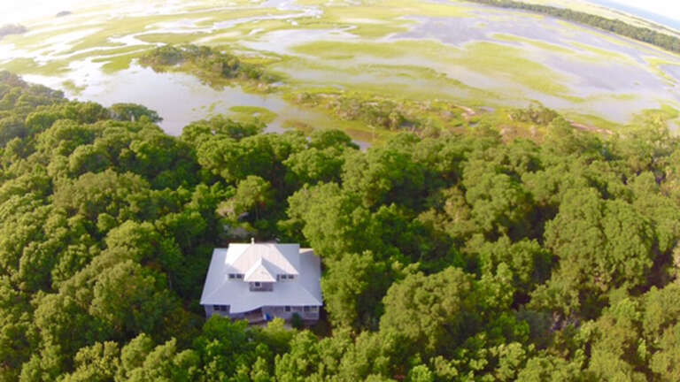 Aerial View Of A Secluded House Nestled In Lush Greenery Near A Marsh