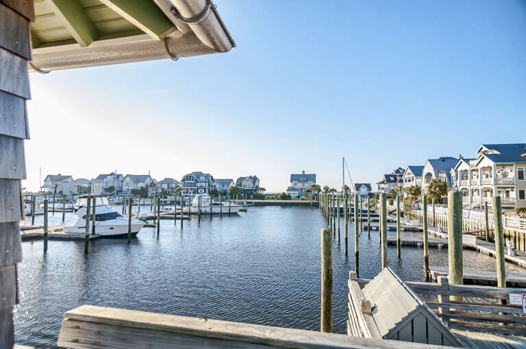 View From A Balcony Overlooking Serene Sea With Boats And Buildings Under Blue Sky