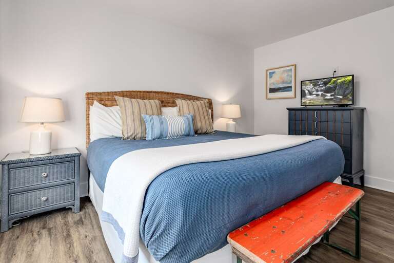 Bed With Blue Bedding, Wicker Headboard, Orange Bench, Lamps On Nightstands