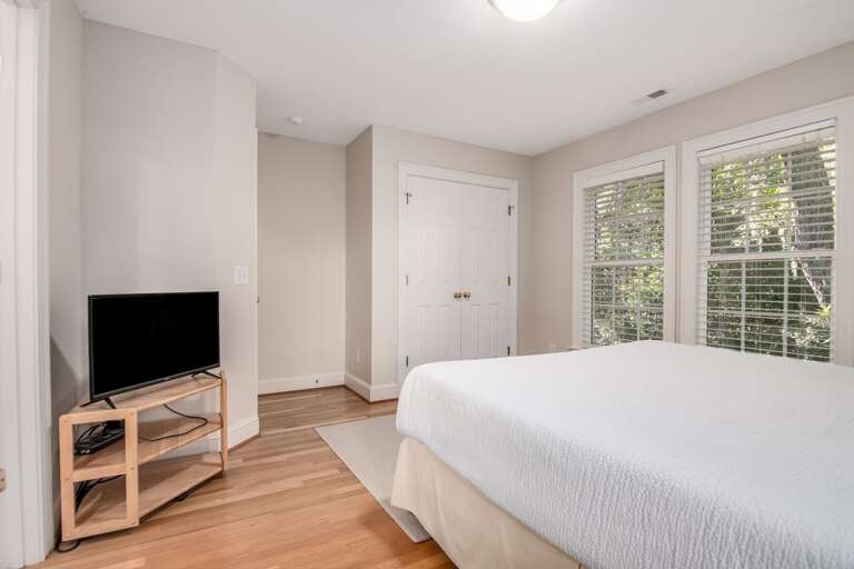 Minimalist Bedroom With Bright Window, White Bedding, And Wooden TV Stand